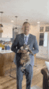 a man in a suit and tie is holding a cat in a living room .