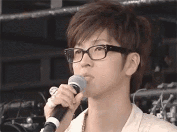 a young man wearing glasses is holding a microphone in his mouth .