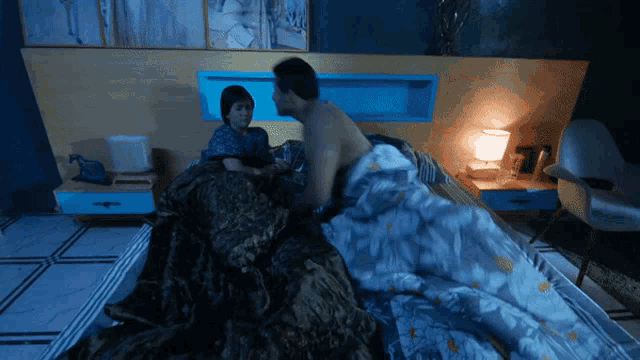 a man and a woman are laying on a bed with a blue headboard