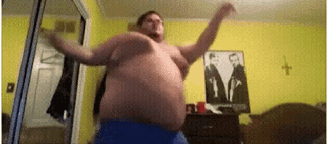 a man with a large belly is dancing in a room with a picture of two men on the wall .