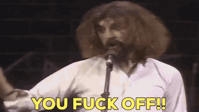 a man with a beard is singing into a microphone and saying " you fuck off "