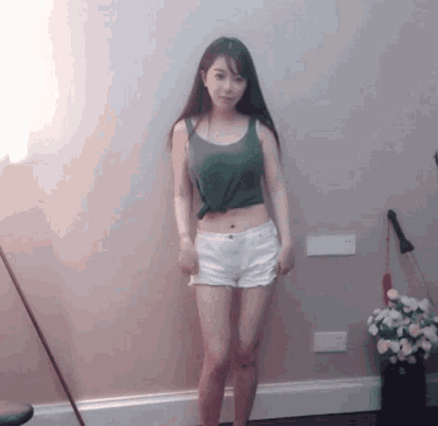 a young woman in a green tank top and white shorts is standing in a room .