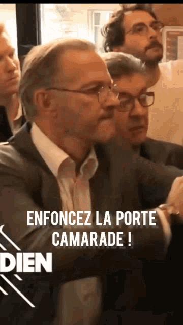 a man in a suit stands in front of a sign that says " entourez la porte camarade ! "