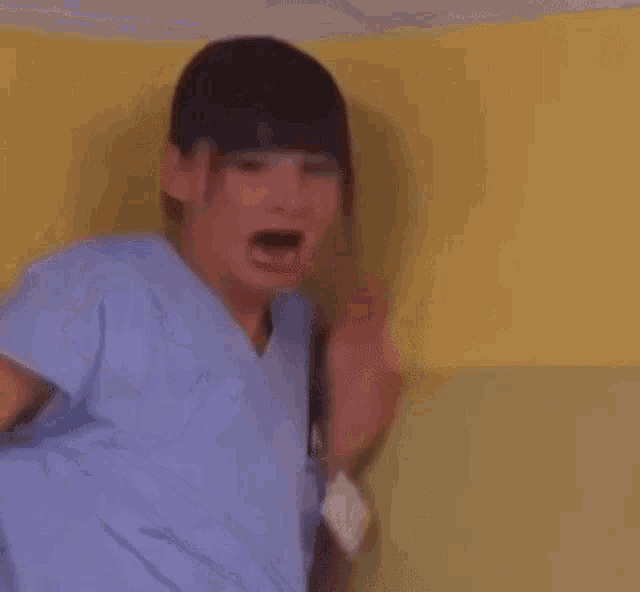 a woman in a blue shirt is standing in front of a yellow wall and making a funny face .