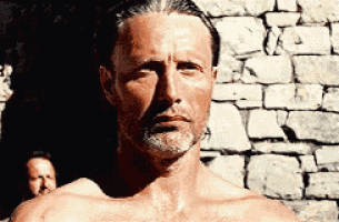 a shirtless man is standing in front of a brick wall .