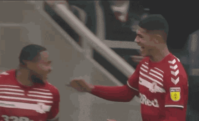 two soccer players are standing next to each other and one of them is wearing a red jersey with the word red on it .