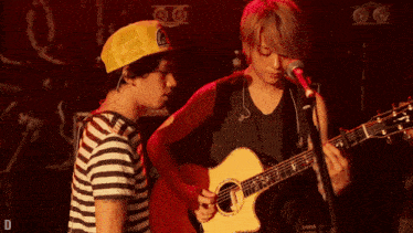 a man singing into a microphone while another man plays guitar