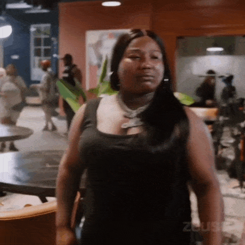 a woman in a black tank top is standing in a room with a lot of people .