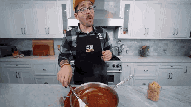a man in a kitchen wearing an apron that says " what tastes like plant based spaghetti "