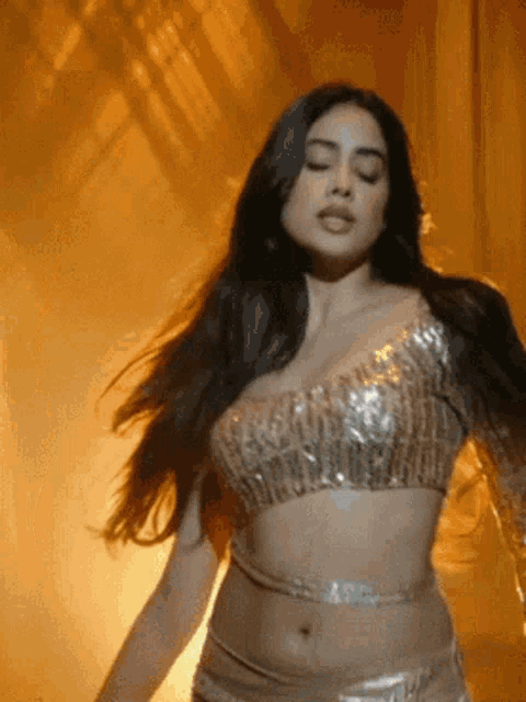 a woman in a crop top is dancing with her eyes closed in a dark room .