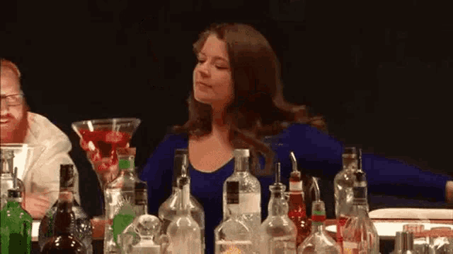 a woman is sitting at a bar surrounded by bottles of liquor .