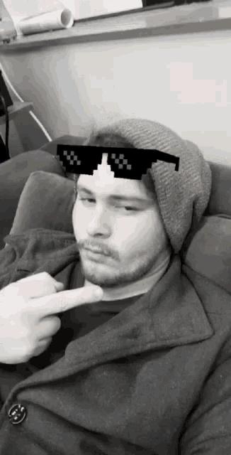a man wearing a beanie and sunglasses is pointing his finger