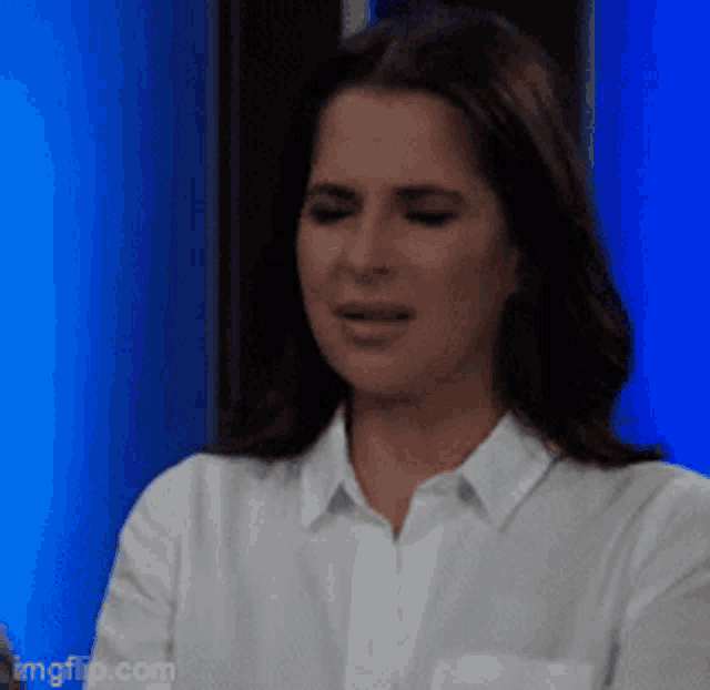 a woman in a white shirt is crying in front of a blue background ..