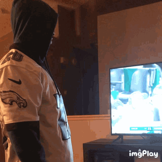 a man wearing a philadelphia eagles jersey watches a game on tv