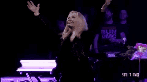 a woman is standing on a stage with her arms outstretched and a sign that says run dmc in the background