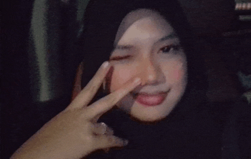 the girl is wearing a hijab and making a peace sign .