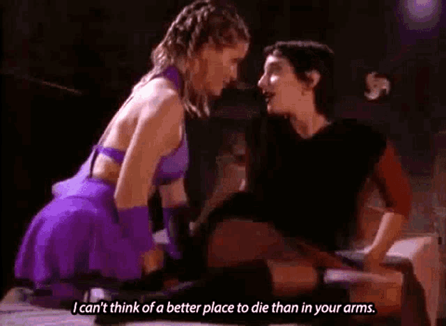a woman in a purple dress is kneeling down next to a man in a black shirt and talking to him .