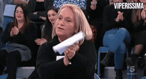 a woman is holding a piece of paper in front of a crowd while sitting in a stadium .