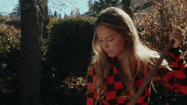 a woman wearing a red and black checkered shirt is holding a rake