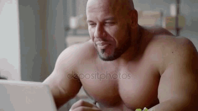 a shirtless muscular man is using a laptop computer while sitting at a table .