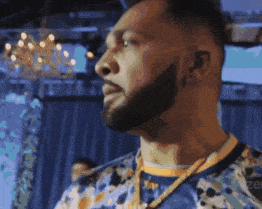 a man with a beard wears a blue shirt and gold chains