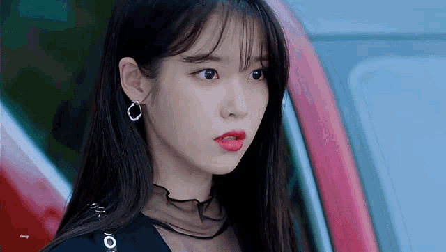 a close up of a woman wearing red lipstick and earrings standing next to a car .