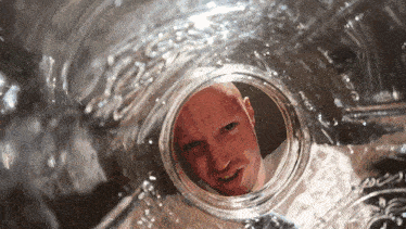 a bald man is looking through a hole in a glass bottle