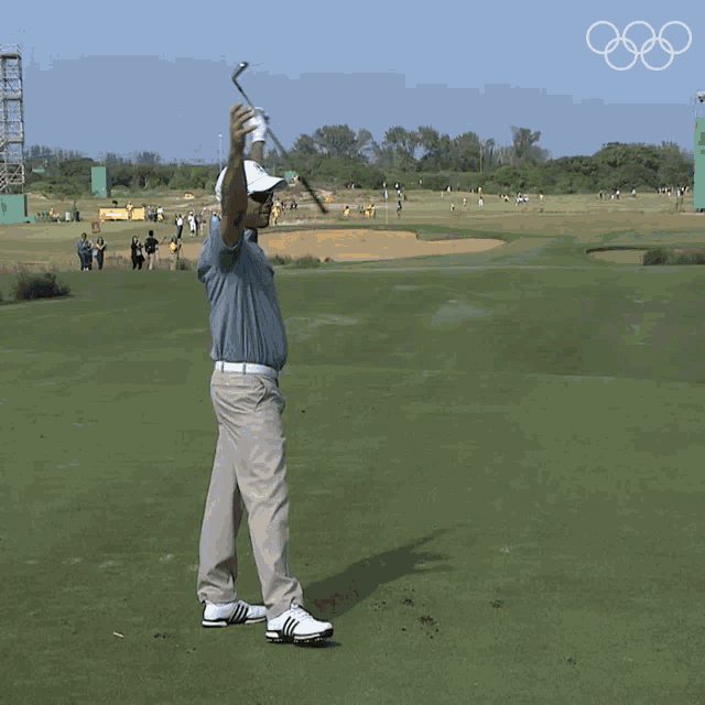 a man is standing on a golf course with his arms up in the air