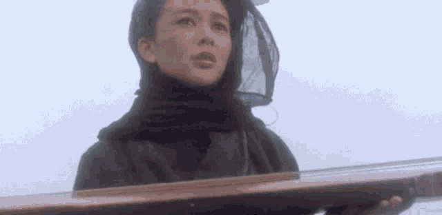 a woman wearing a black scarf and a veil is holding a wooden box .