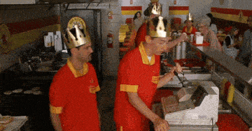 two men wearing crowns are working at a hot dog stand