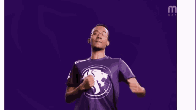 a man wearing a purple shirt with a lion on it is dancing on a purple background .