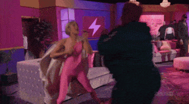 a woman in a pink bodysuit is fighting a man in a green jacket in front of a sign that says zeusz