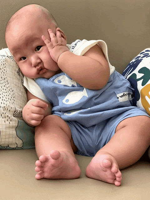 a baby wearing a blue shirt with fish on it is sitting on a pillow