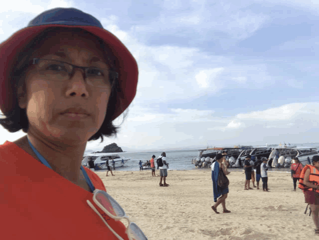 a woman wearing glasses and a red hat stands on the beach