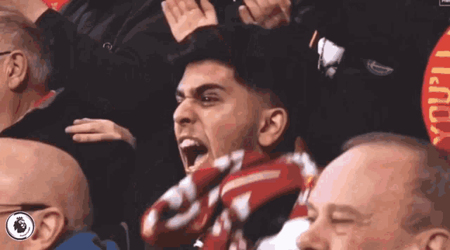 a man with a scarf around his neck is screaming in a crowd of people