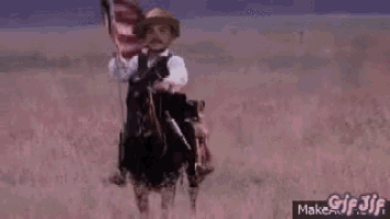 a man in a cowboy hat is riding a horse in the desert while holding a flag .