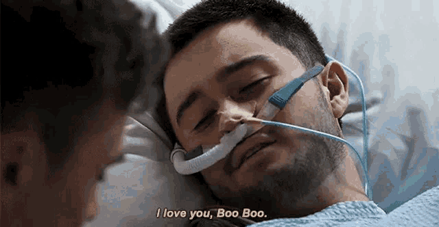 a man in a hospital bed with an oxygen mask on his face is talking to another man .
