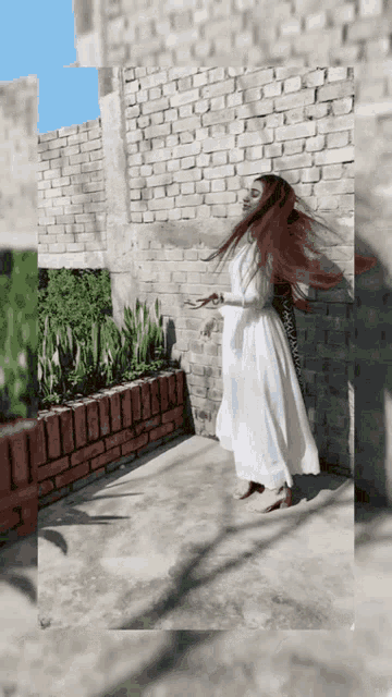 a woman in a long white dress is standing in front of a brick wall