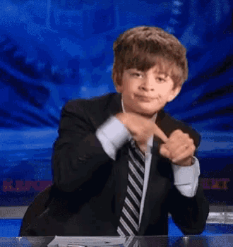 a boy in a suit and tie is sitting at a desk
