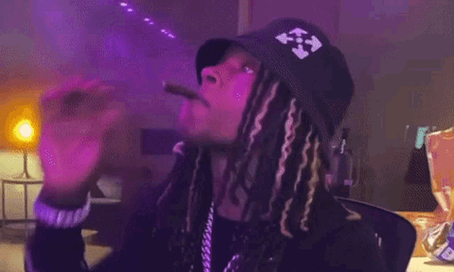 a man with dreadlocks is smoking a cigar in a room with purple lights behind him .
