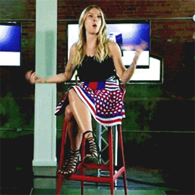 a woman wearing a red white and blue skirt is sitting on a stool