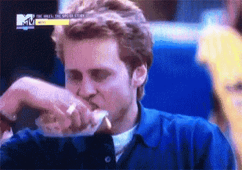 a man in a blue shirt is eating a hot dog with a mtv logo in the background