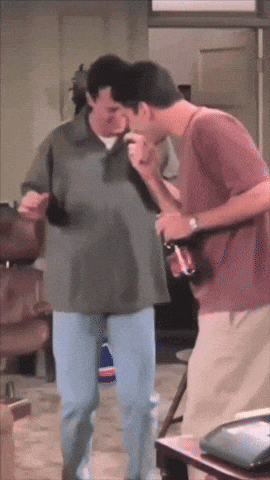 two men are standing next to each other in a living room and one is holding a guitar