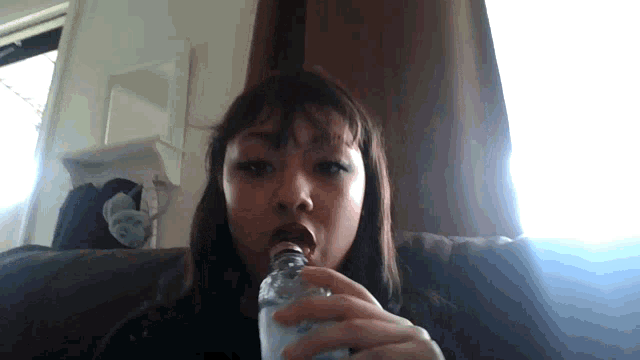 a woman sitting on a couch drinking from a bottle