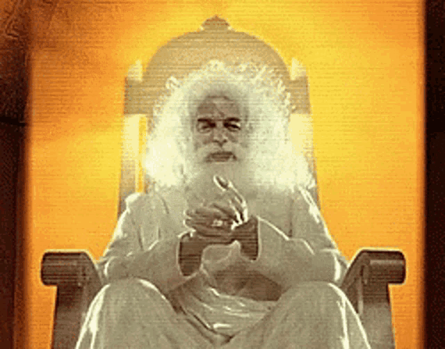 a man with white hair and a beard is sitting in a chair with his hands folded
