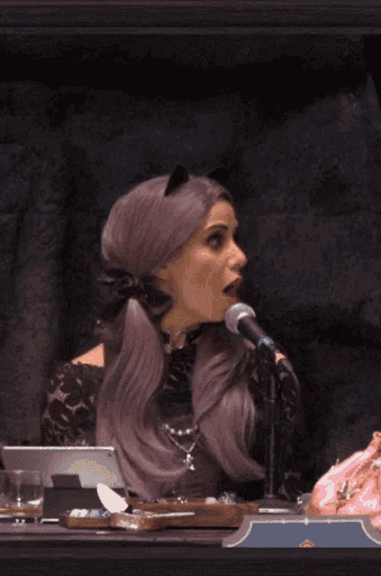 a woman with purple hair is sitting in front of a microphone with her mouth open