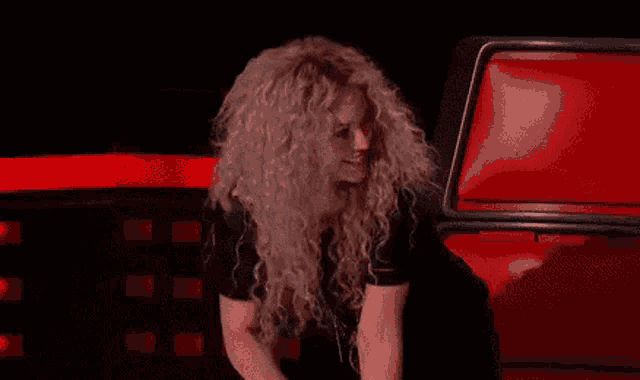shakira is smiling while sitting in a red chair on the voice .