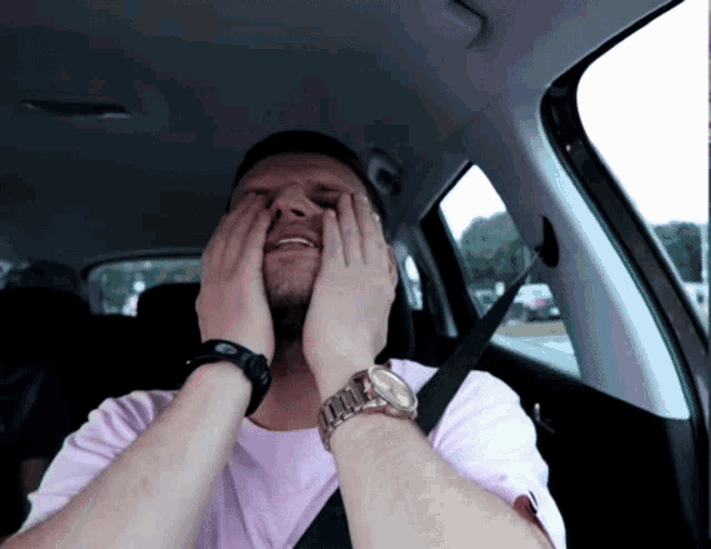 a man wearing a watch and a pink shirt is covering his face in a car