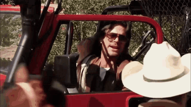 a man wearing sunglasses and a cowboy hat is sitting in a red truck .