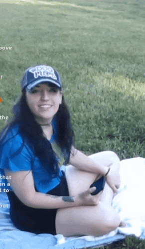 a woman wearing a hat with the word titans on it is sitting on a blanket in the grass